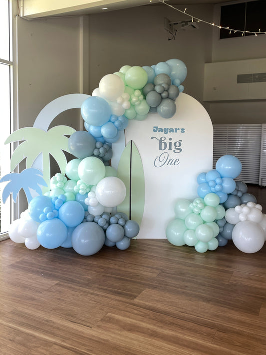 Balloon arch with 'Angus's big One' text in a room with large windows.