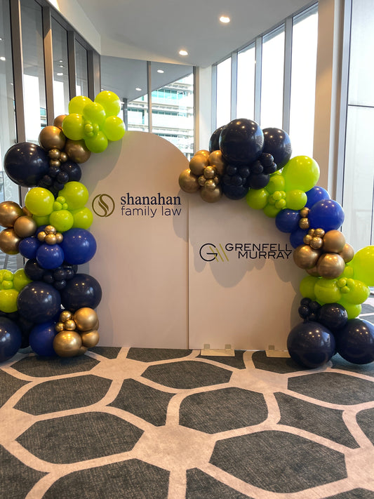 Decorative wreath made of balloons on a branded box with a patterned wall in the background.